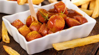 Currywurst mit Pommes in weißer Schale, mit Currypulver bestreut – Insider-Tipp: Curry 36.